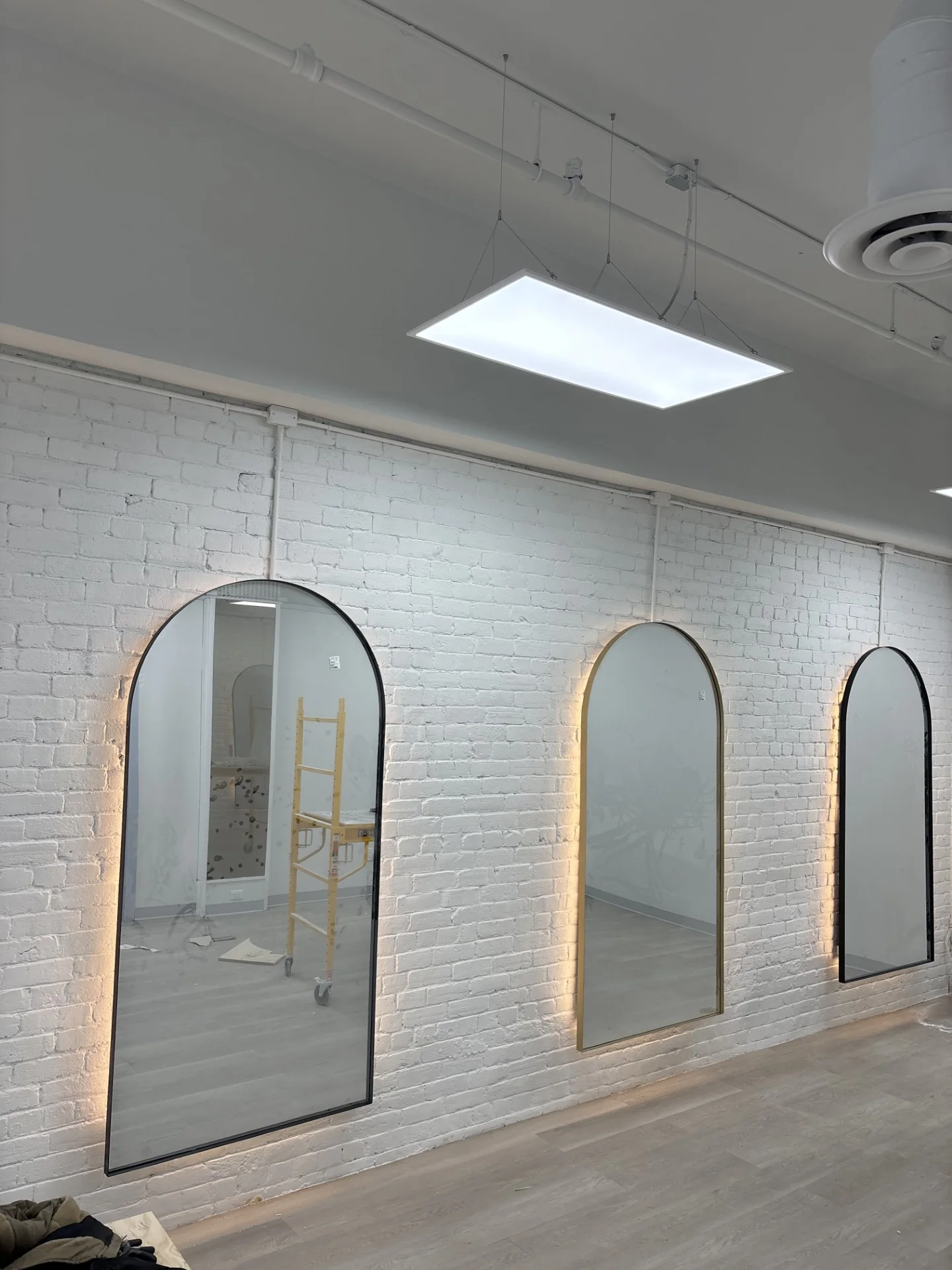 Arched mirrors with warm backlighting against a white brick wall