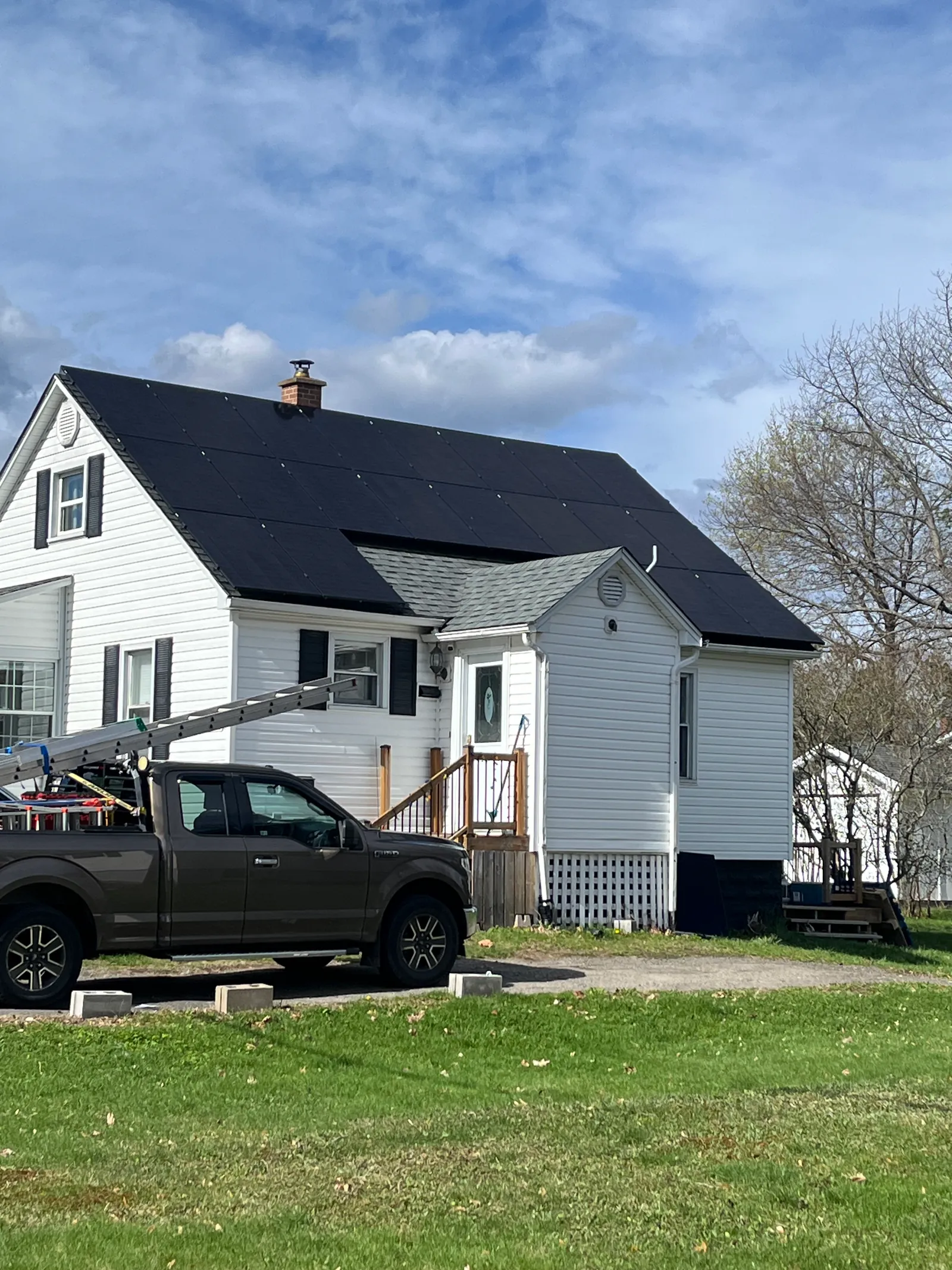 Black solar panels across the roof of a white house, with the work vehicle in front